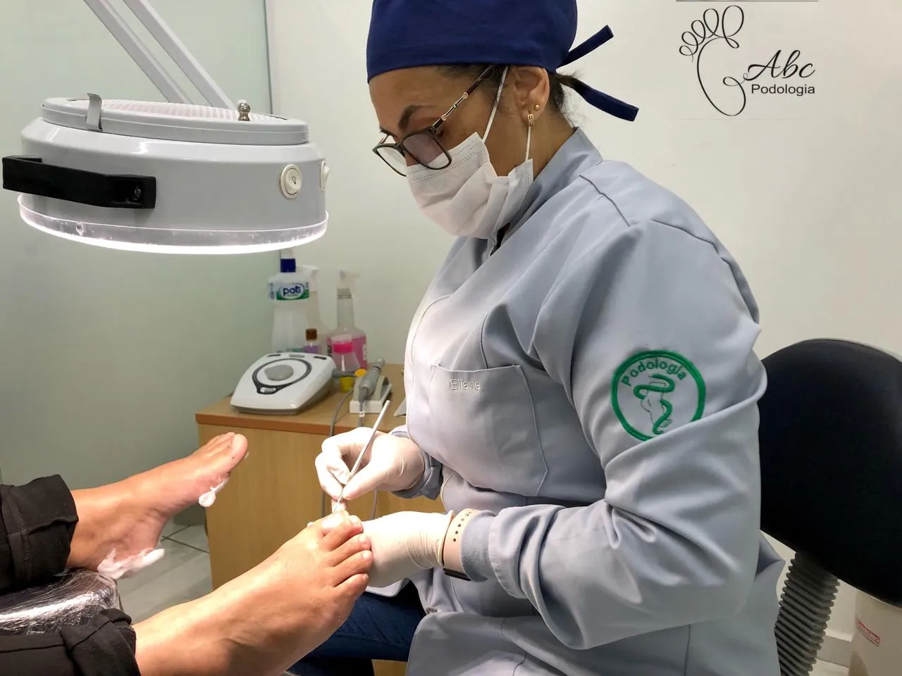 Podóloga da Podologia ABC atendendo uma paciente em consultório, com instrumental esterilizado e luz clínica